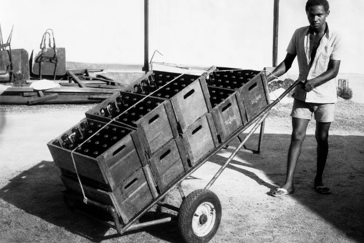 Trabalhador transportando caixas de garrafas em um carrinho.